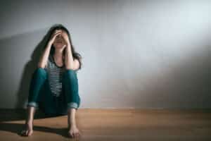 A woman with bipolar disorder sitting on the floor with her head in her hands