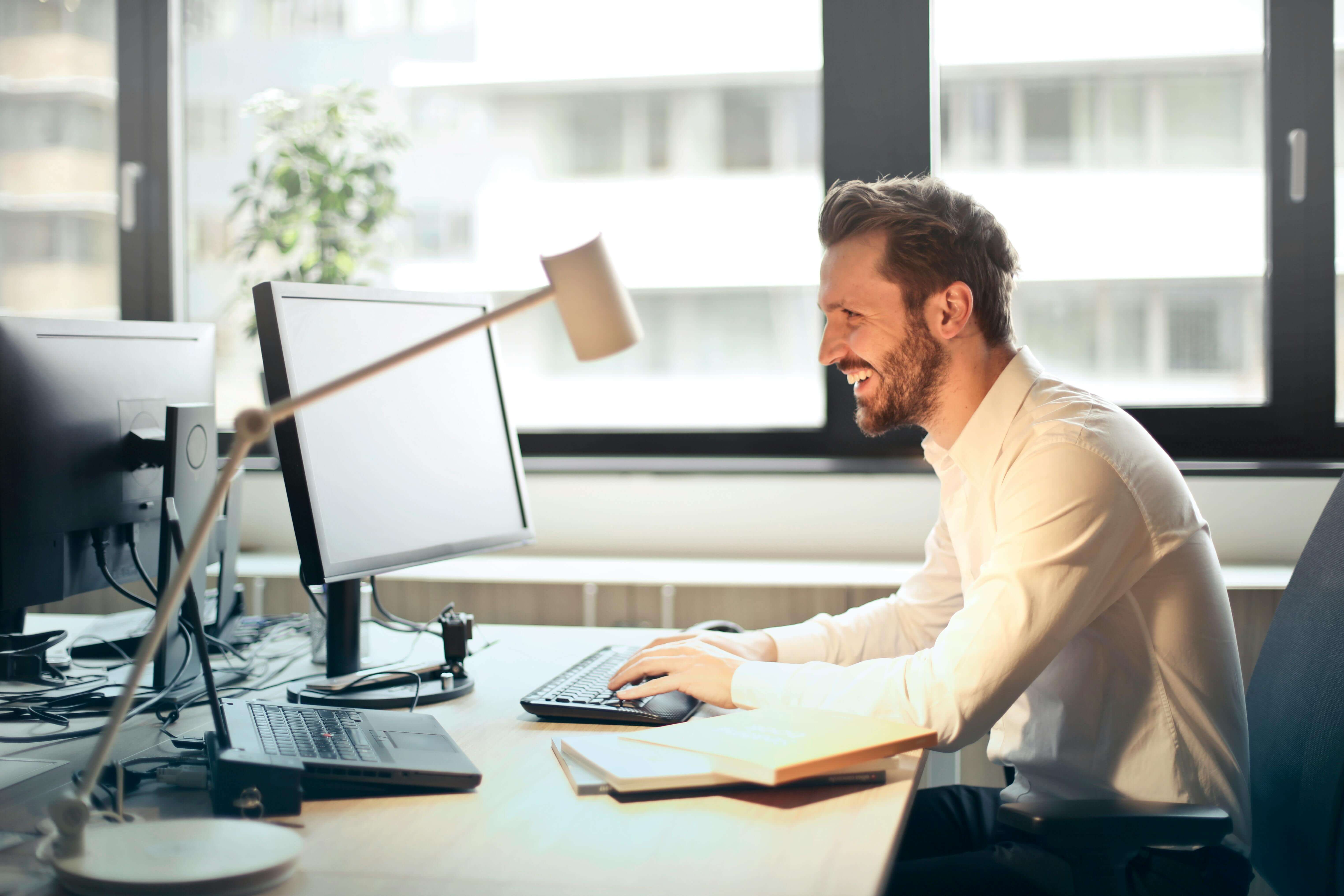 A professional man smiling while working at his desk in a bright office. Begin finding balance and inner peace as a high-performing man with men’s therapy in Kenosha, WI where a skilled men’s therapist helps address men’s anxiety and stress.