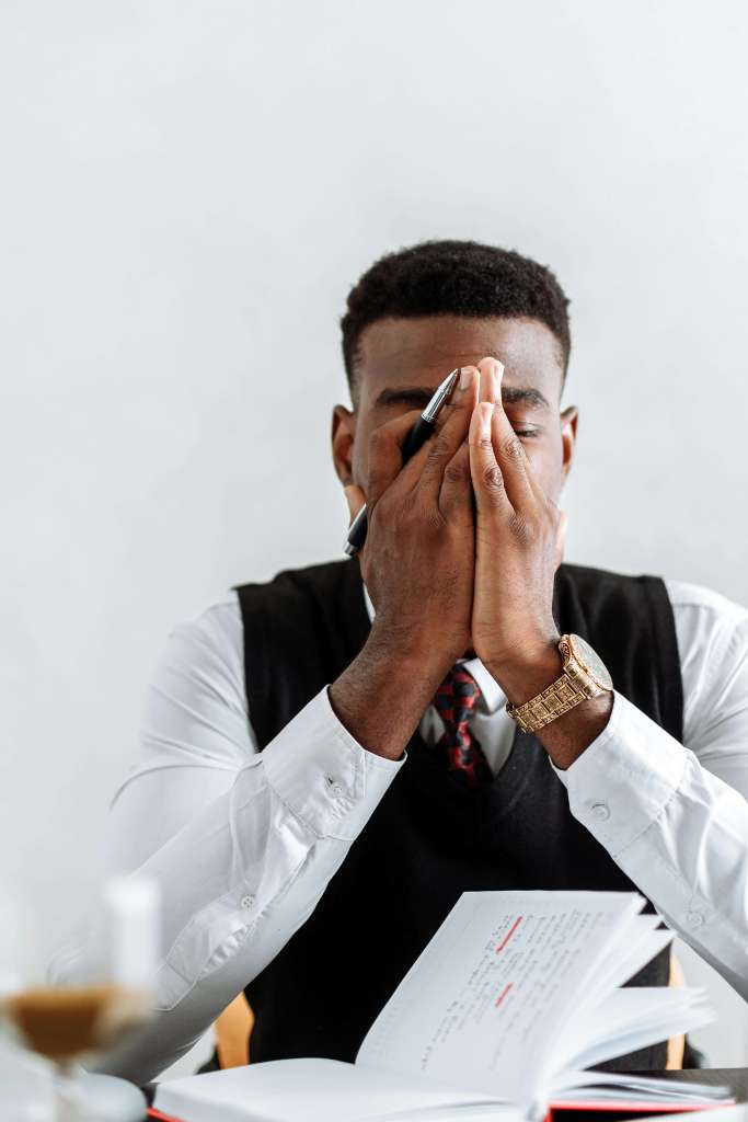 An overwhelmed professional man sits at a desk with his hands covering his face. Begin healing from burnout and pressure through men’s therapy in Kenosha, WI where men’s anxiety and performance stress are understood and supported.