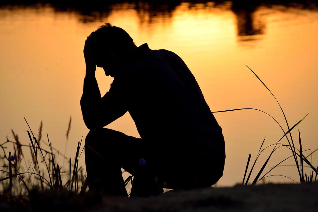 A silhouette of a man sitting by a body of water at sunset, leaning forward with one hand on his head. Don't go through life trying to hold on. Find support with men's therapy in Kenosha, WI to begin coping in healthy ways.