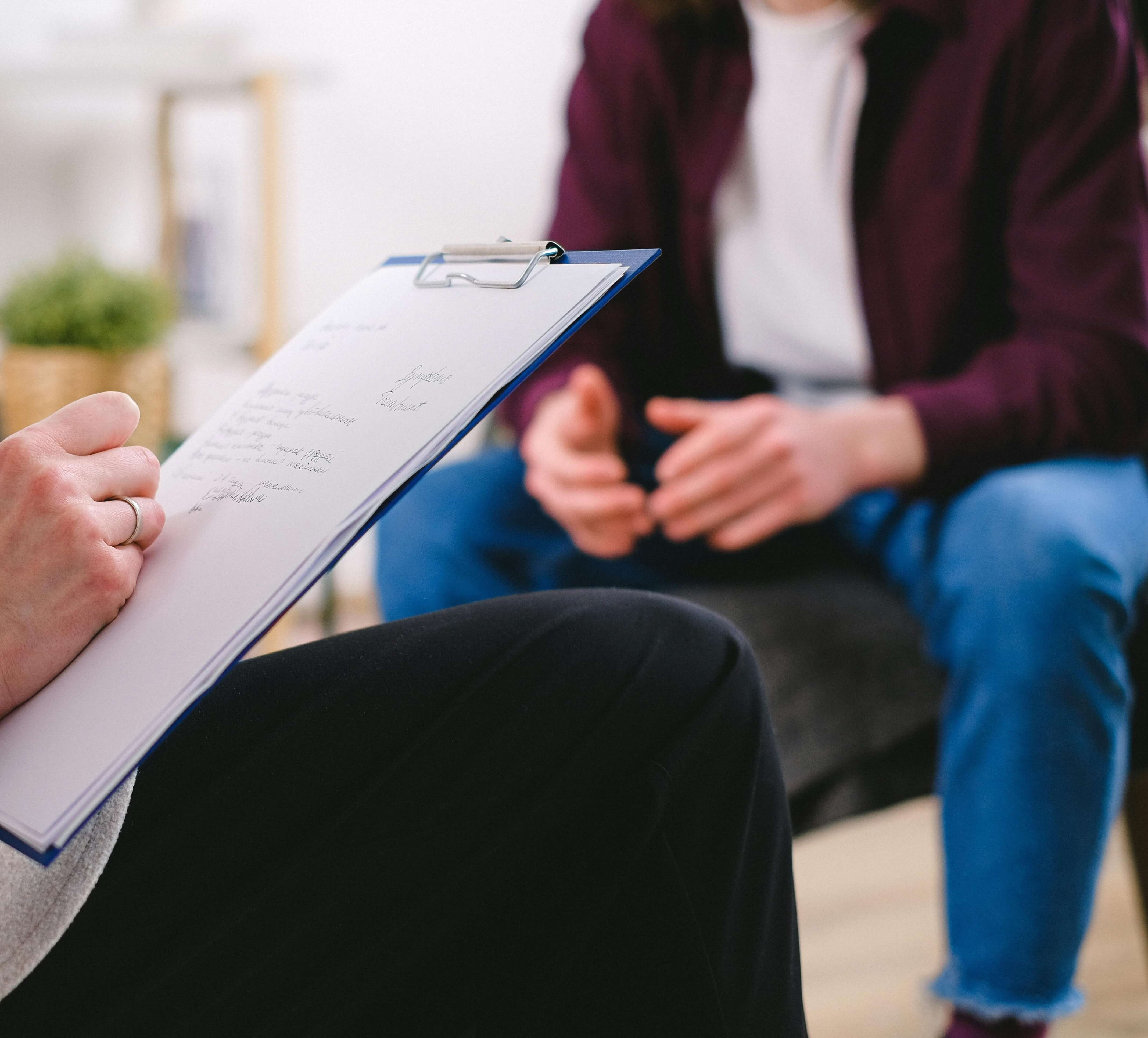 man in therapy | men and grief in milwaukee, wi | mens therapy | mens therapist | Racine | Milwaukee | Madison A therapist holding a clipboard while sitting across from a man during a counseling session. Men seeking clarity and emotional balance after loss can benefit from men's therapy in Milwaukee, WI focused on grief recovery.