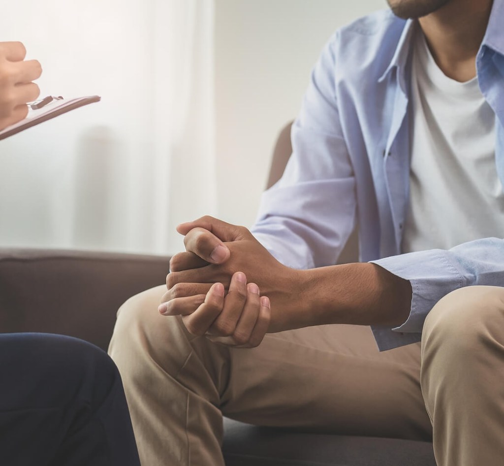 Man seated with hands clasped, listening attentively during a therapy session. Men's therapy in Milwaukee, WI supports men in processing trauma symptoms that affect sleep, mood, and emotional regulation.