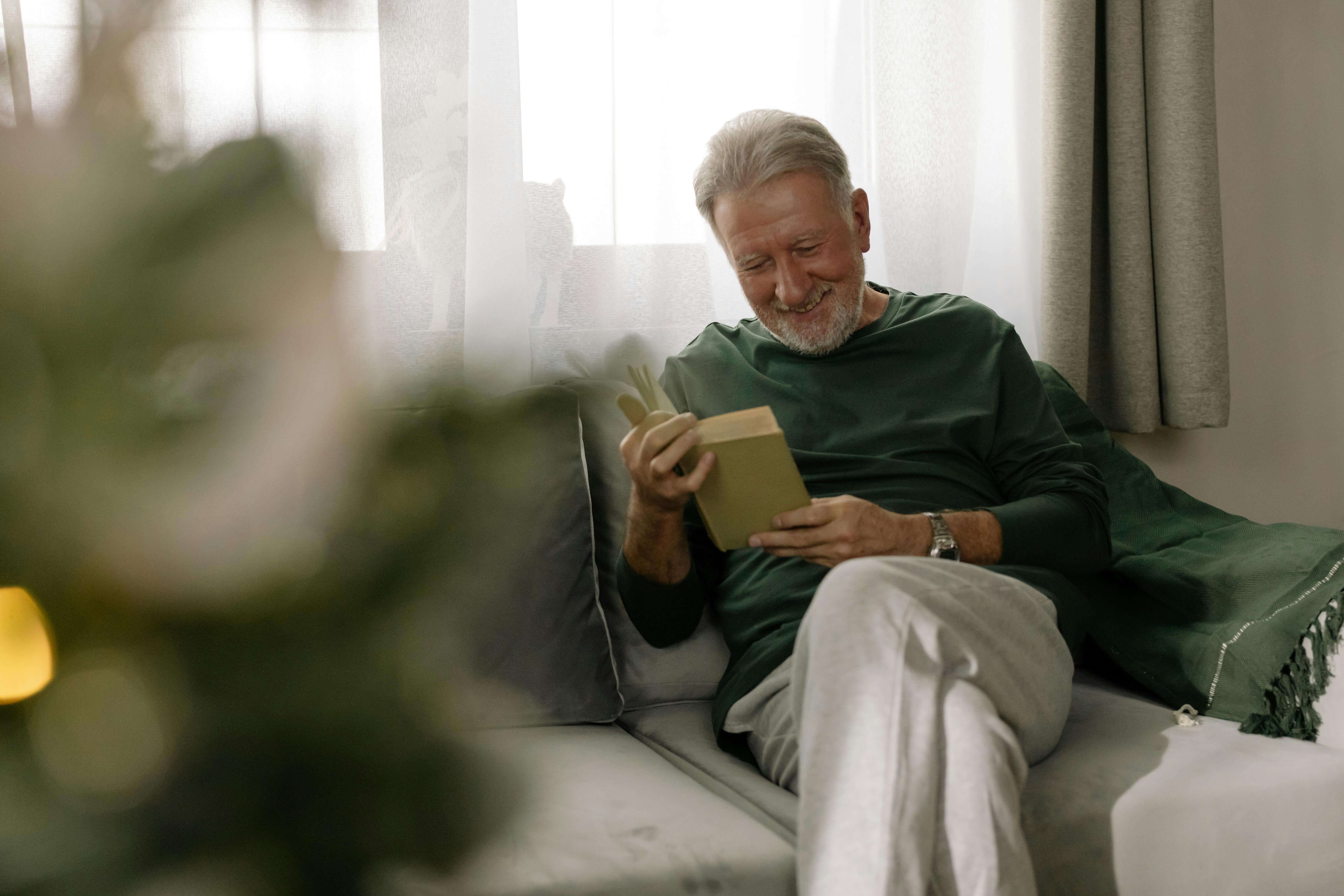 book | mens trauma therapy in milwaukee, wi | men and mental health | male mental health | Mount Pleasant | Burlington | Lake Geneva An older man relaxes on a couch while reading a book near a window with soft natural light. Men’s therapy in Milwaukee, WI helps men heal trauma so they can feel calmer, more present, and grounded in daily life.