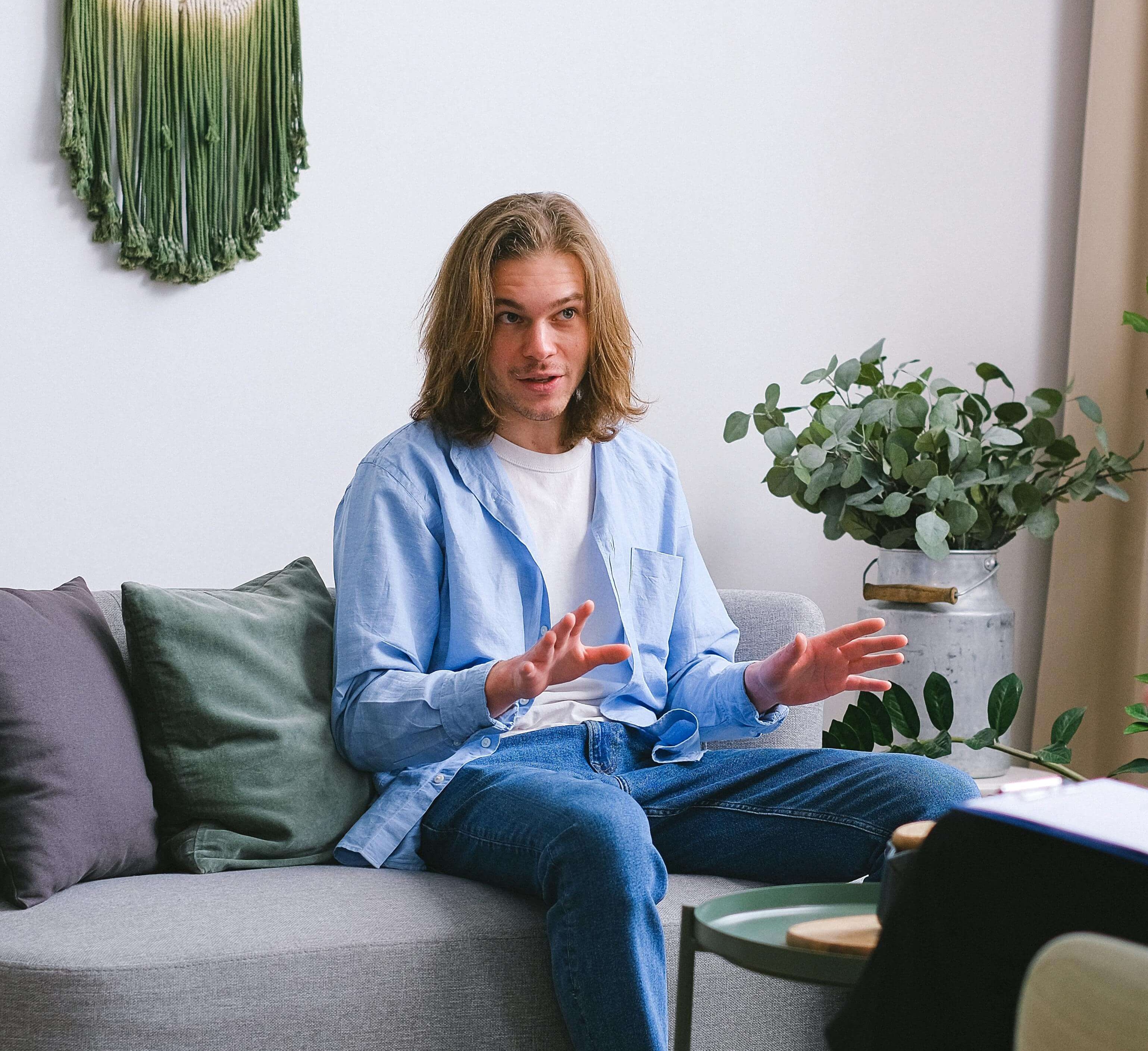 man in therapy | male therapist in milwakee, wi | mens therapy | men and mental health | Mount Pleasant | Burlington | Lake Geneva Man sitting on a couch during a therapy session, gesturing with his hands while speaking. Through mens therapy in Milwaukee, WI, men can safely talk through trauma and begin restoring balance in their daily lives.
