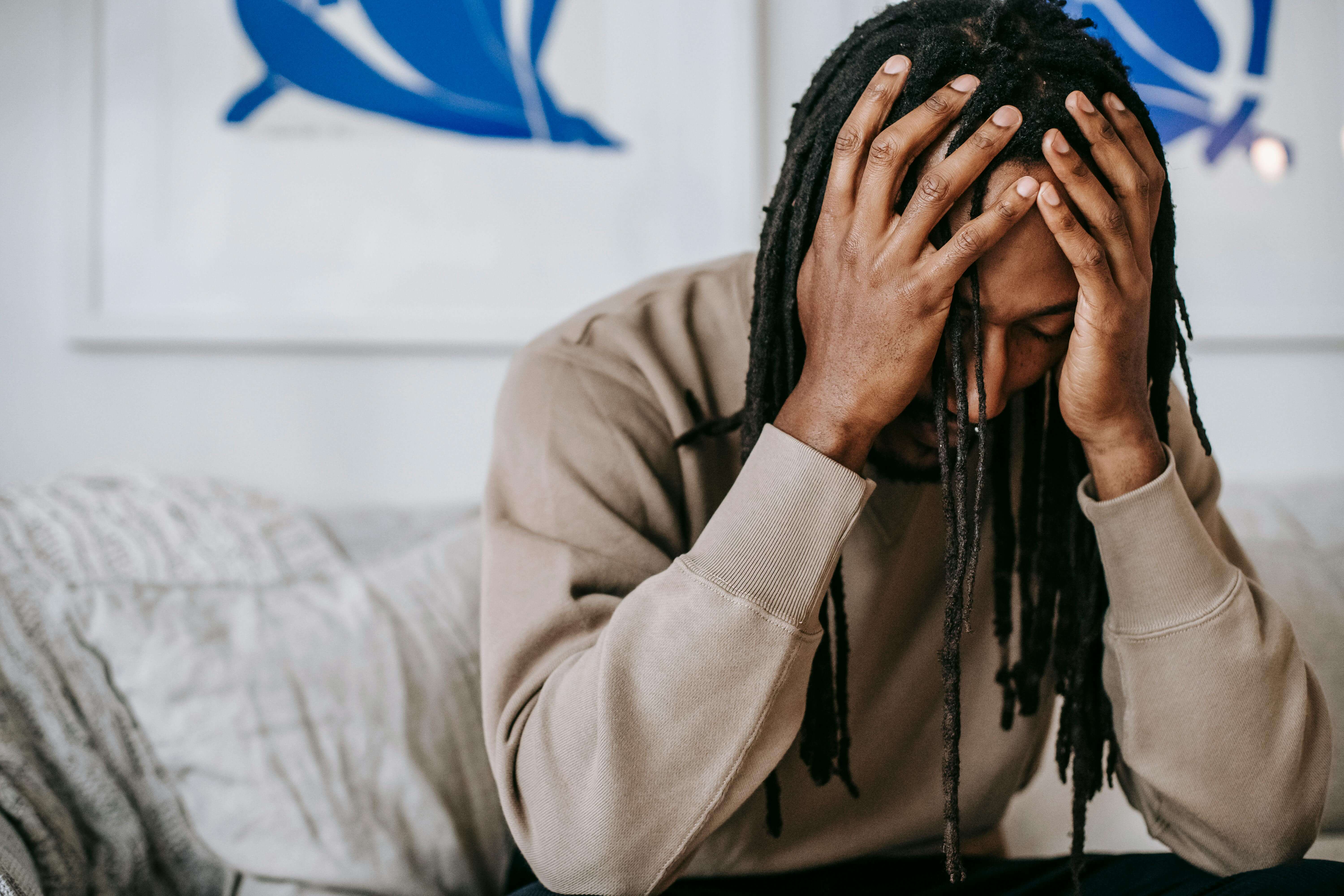 Man with locs sitting on couch with hands covering his face in distress. High-functioning anxiety keeps many men trapped in internal chaos, but men's therapy in Milwaukee, WI helps you find peace without losing your edge.