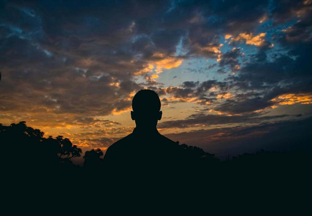Silhouette of a man against a sunset sky with dramatic clouds. Find space to process unresolved grief with grief counseling for men in Milwaukee, WI.