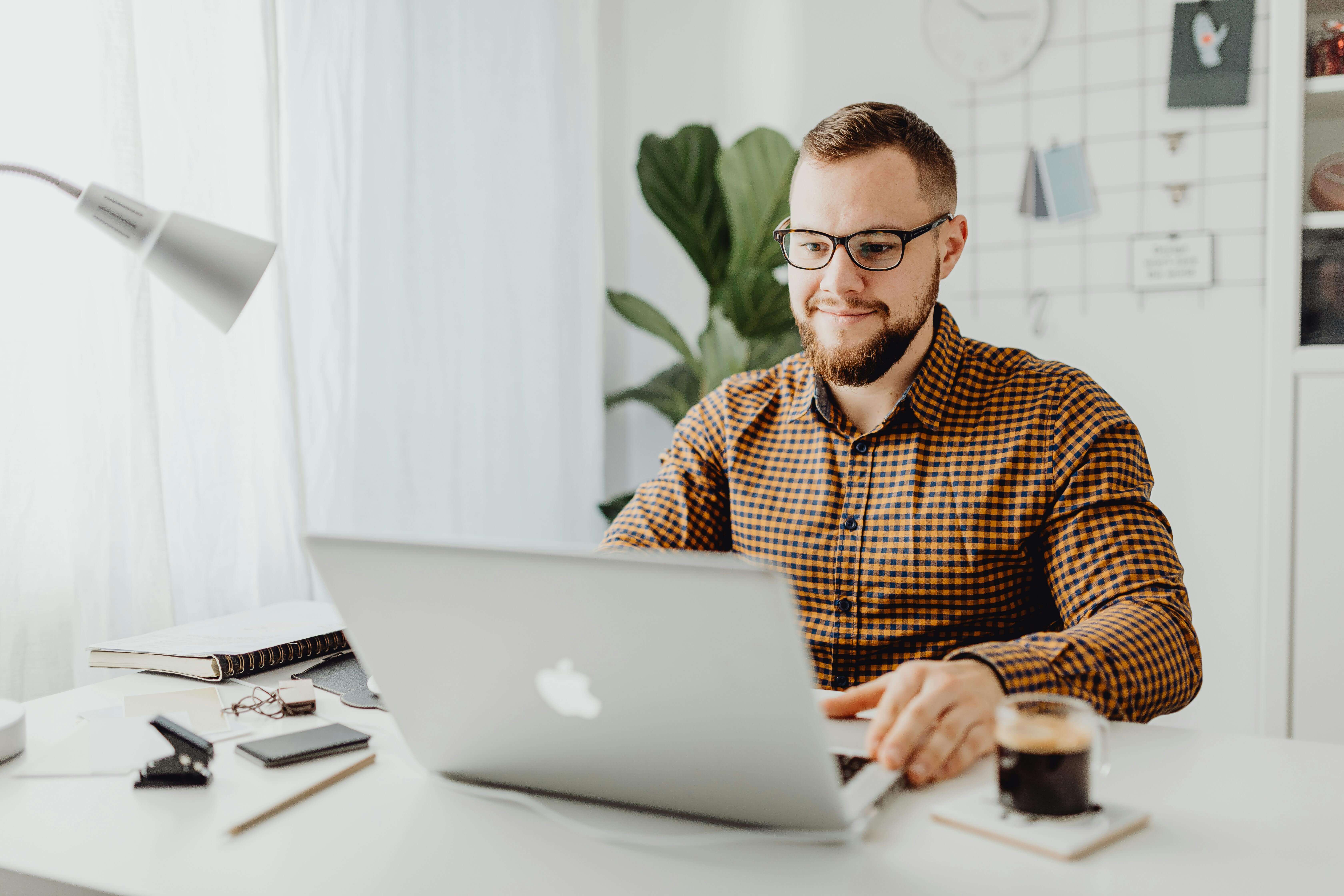 Man in checkered shirt working on laptop at home office desk. Break free from anxiety and build the life you want with men's therapy in Milwaukee, WI.
