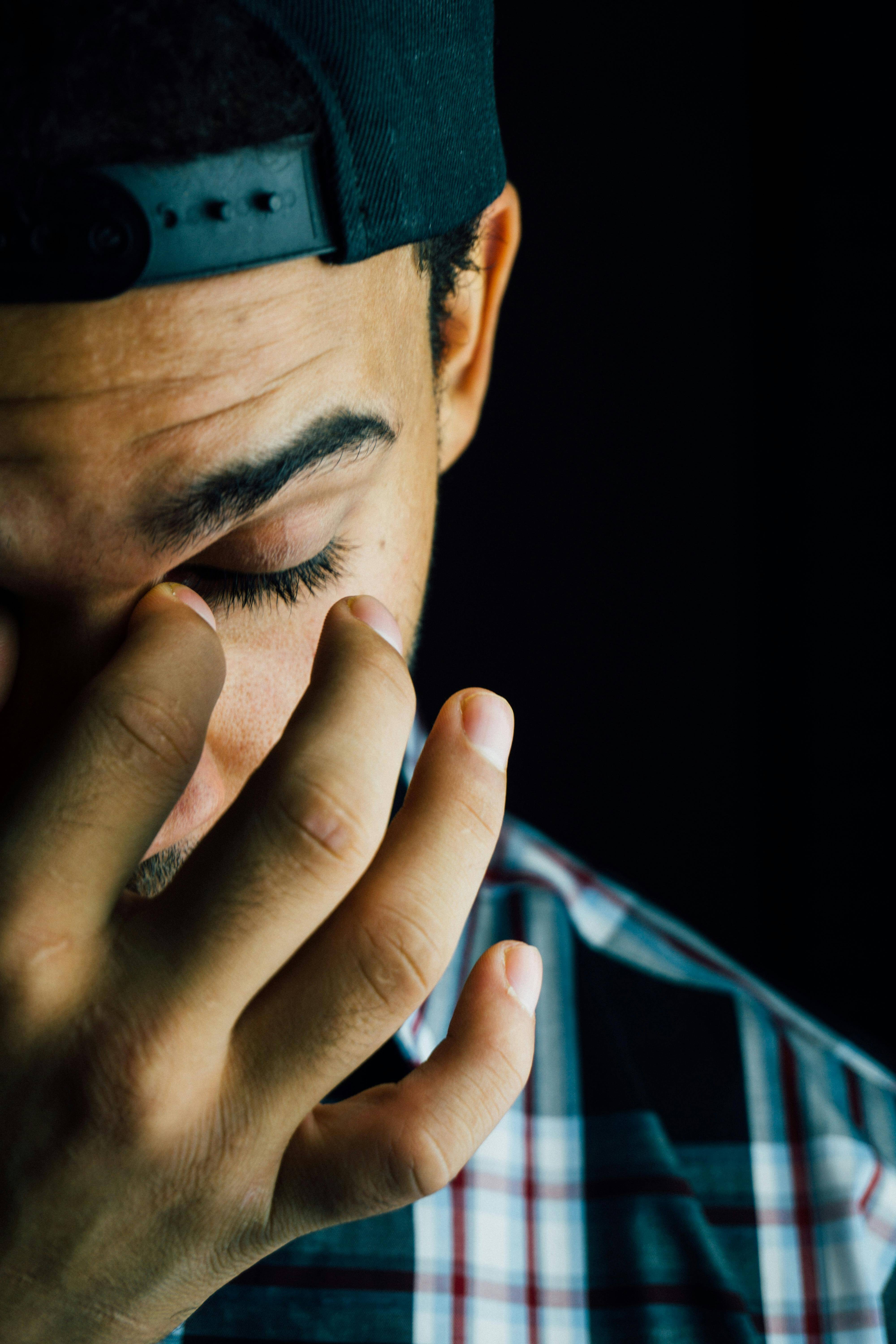 Man in baseball cap with hand covering face showing distress. Find relief from overwhelming emotions through men's therapy in Milwaukee, WI.