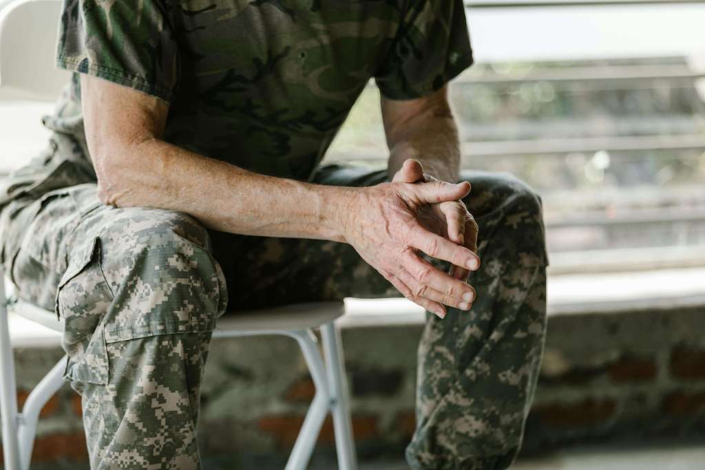 Soldier in camouflage uniform sitting with clasped hands showing contemplation and stress. Heal from PTSD and reconnect with your family through men's therapy in Milwaukee, WI.