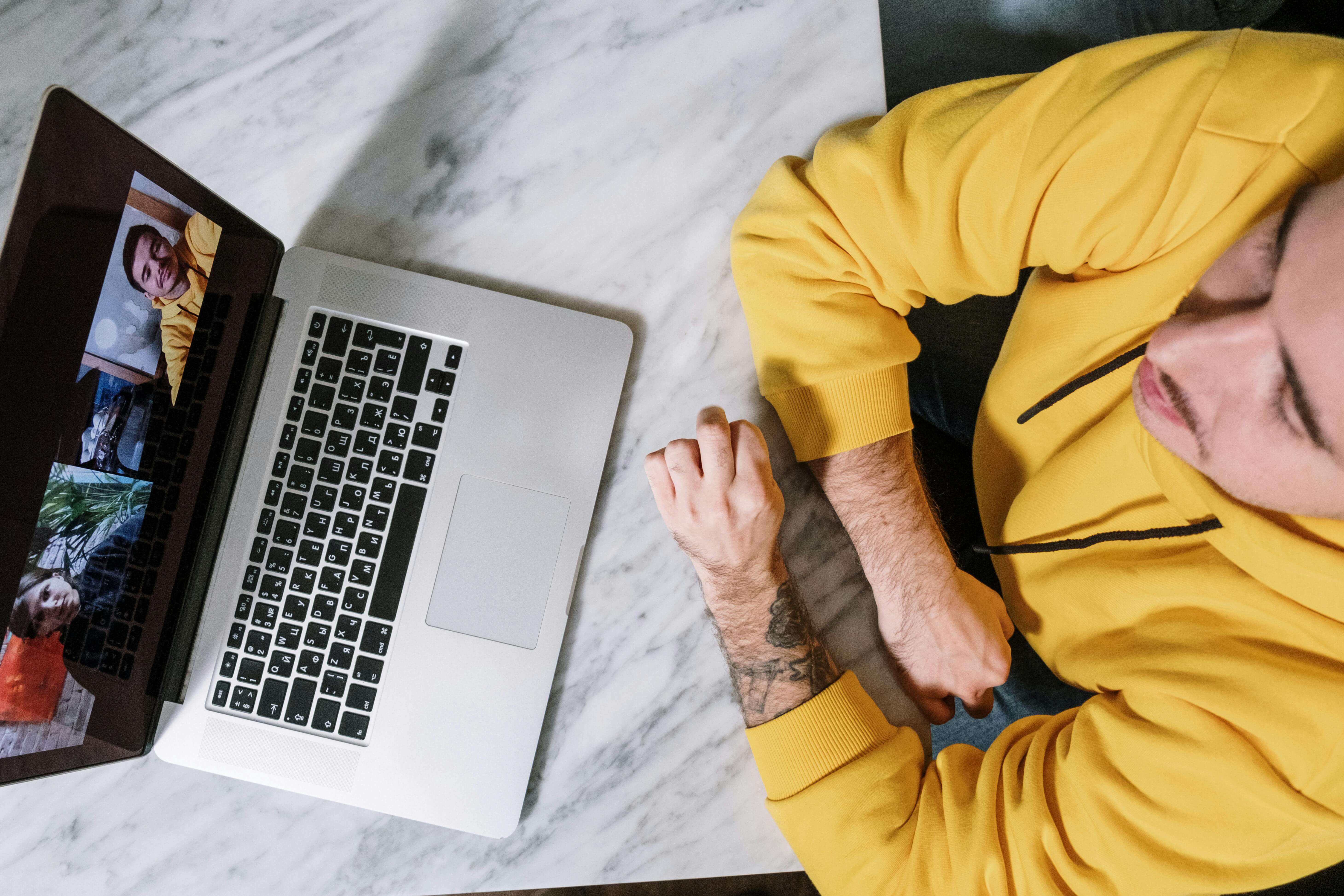 Overhead view of man in yellow sweatshirt sitting at a table near laptop during video call. Heal from entrepreneurial burnout, betrayal, and trauma responses with somatic approaches in men's therapy in Milwaukee, WI.