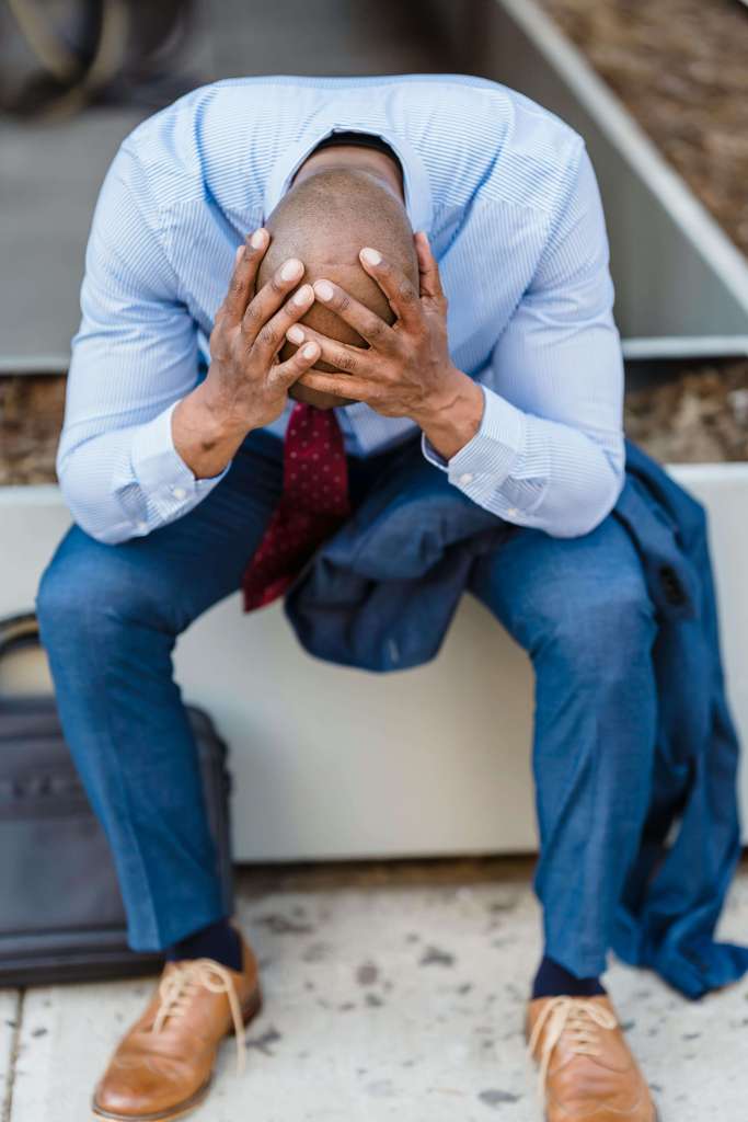 Man in blue dress shirt and tie sitting on bench with head in hands looking down. Process entrepreneurial stress, betrayal trauma, and overwhelming events stored in your body with men's therapy in Milwaukee, WI.