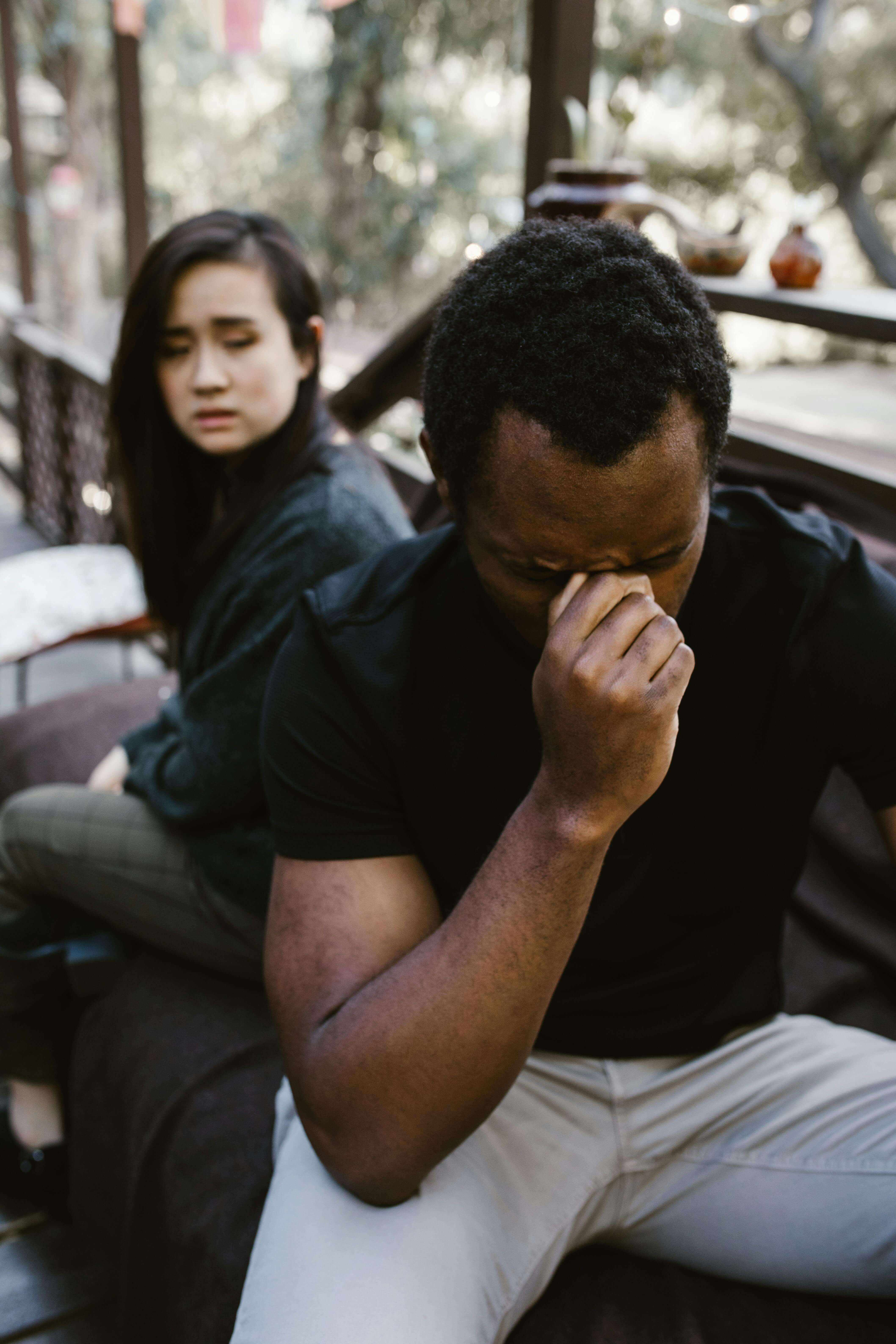 A couple sitting back to back outdoors, both looking distressed and avoiding eye contact. When trust is broken, mens therapy in Milwaukee, WI gives you the tools to heal and move forward.