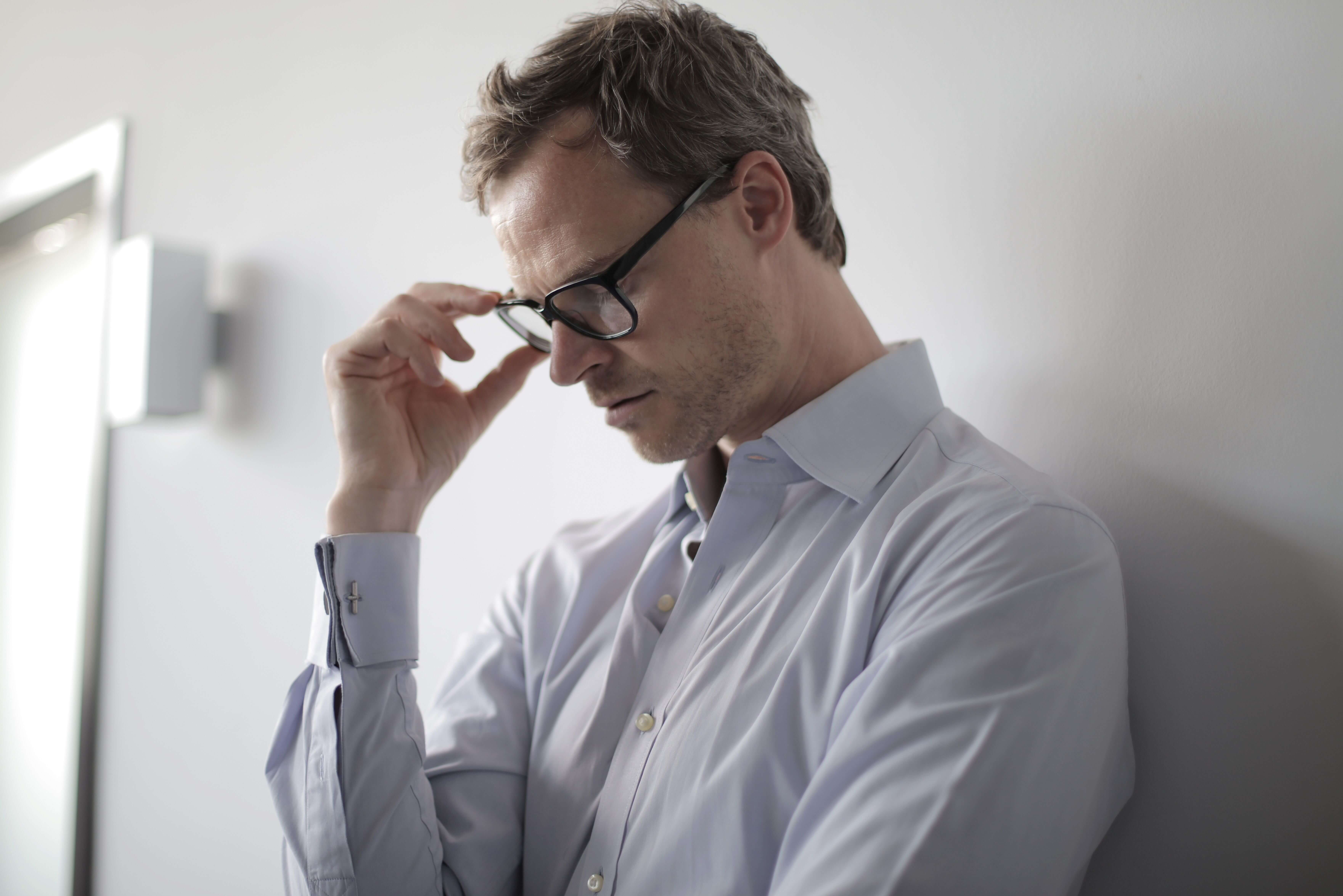 man in dress shirt | trauma therapist in Milwaukee, WI | trauma and anxiety | trauma and depression | Wauwatosa | Brookfield | Pewaukee Man in a light blue dress shirt leaning against a wall with his head down holding his glasses in deep thought. Still trying to figure out which trauma therapy is right for you. Trauma therapy in Milwaukee, WI helps men find the right fit and start healing.