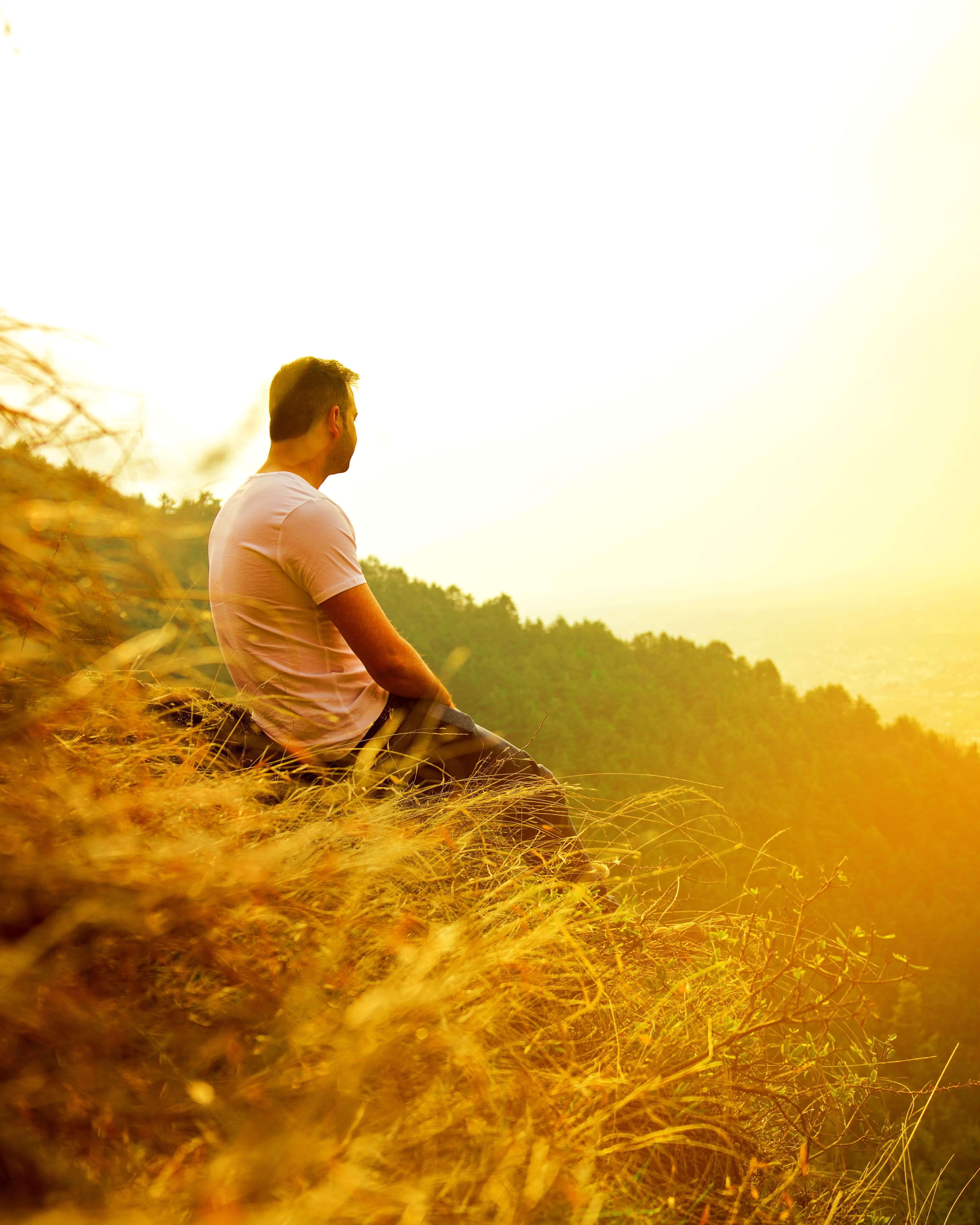 man sitting on golden hillside | trauma therapist in Milwaukee, WI | trauma therapy for men | men and mental health | Wauwatosa | Brookfield | Pewaukee Man in a white shirt sitting on a golden hillside looking out over a glowing sunlit landscape with trees and haze in the distance. Healing from grief and trauma is possible. Trauma therapy in Milwaukee, WI helps men reconnect with peace and purpose after loss.